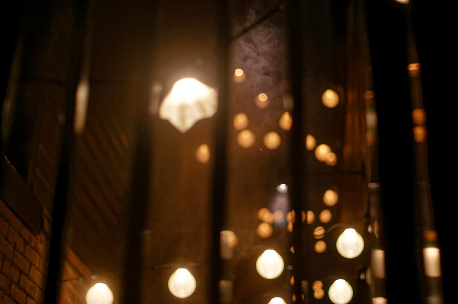 A photo of festoon string lighting through an iron bar fence at nighttime.